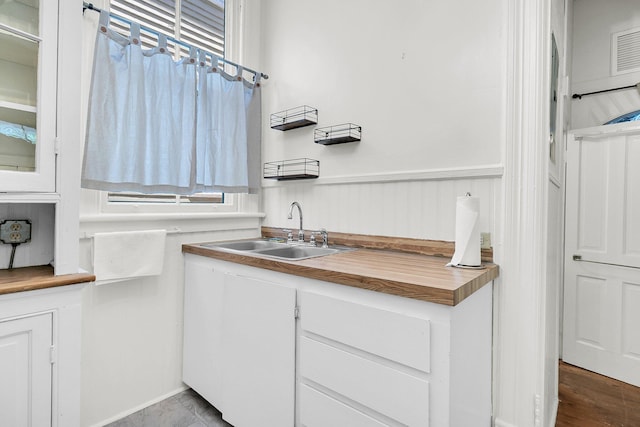 kitchen featuring butcher block counters, glass insert cabinets, white cabinetry, and a sink