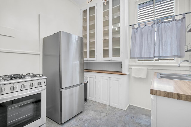 kitchen featuring butcher block counters, a sink, glass insert cabinets, and stainless steel appliances