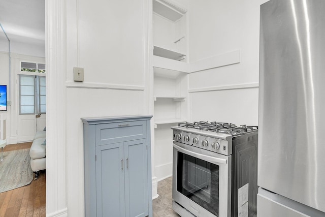 kitchen with stainless steel appliances, light countertops, open shelves, and wood finished floors