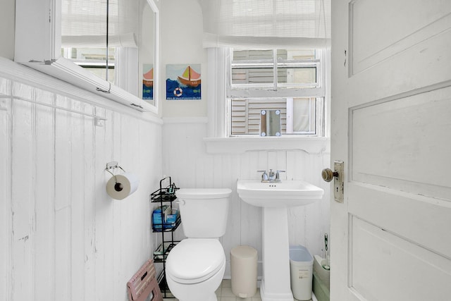 half bathroom with toilet, a decorative wall, a sink, and a wainscoted wall