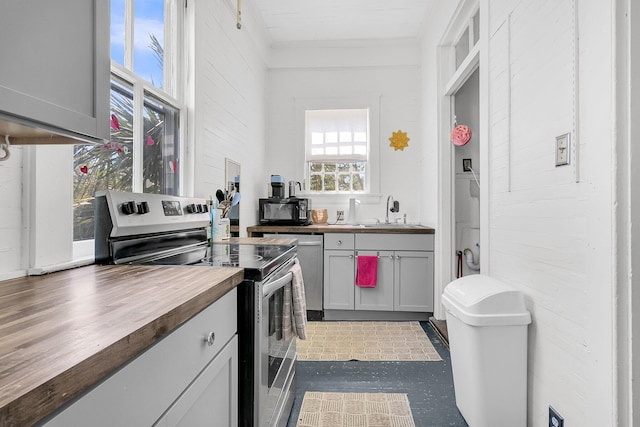 kitchen featuring wood counters, stainless steel range with electric cooktop, a sink, and dishwasher