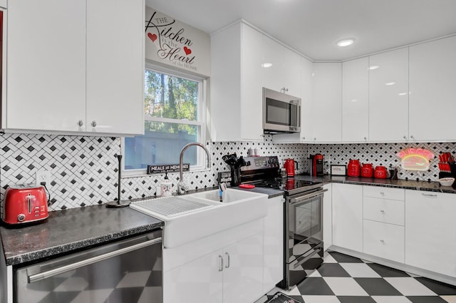 kitchen with appliances with stainless steel finishes, backsplash, dark stone counters, sink, and white cabinetry