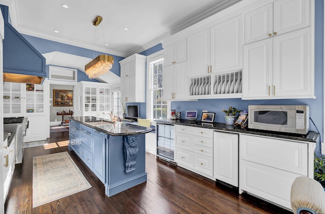 kitchen featuring dark hardwood / wood-style floors, crown molding, white cabinetry, and an island with sink