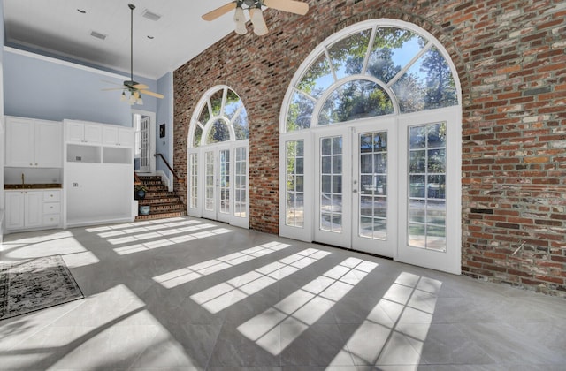 unfurnished living room with french doors, ornamental molding, brick wall, ceiling fan, and a high ceiling