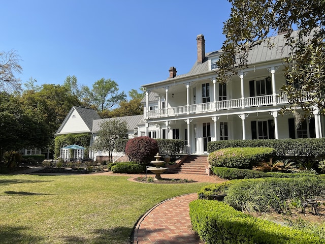 rear view of property featuring a porch, a yard, and a balcony