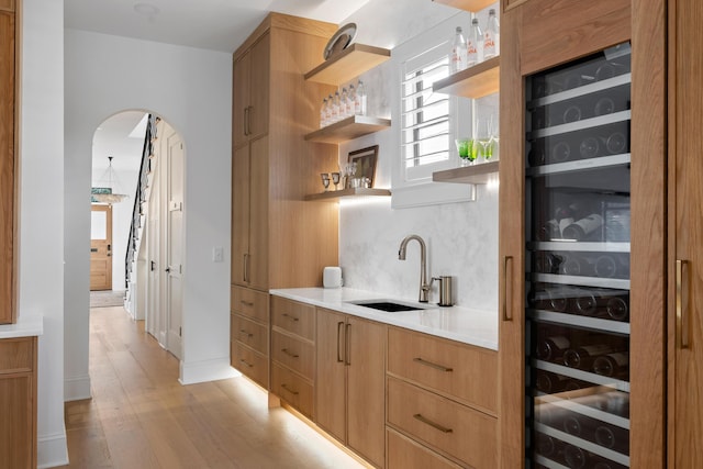 bar featuring light wood-type flooring, tasteful backsplash, arched walkways, and a sink