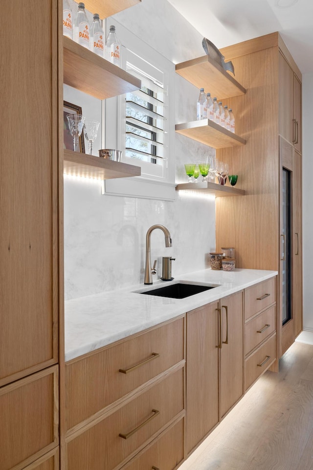 bar featuring light wood-type flooring, backsplash, and a sink