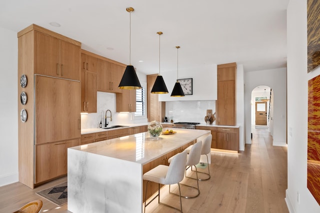 kitchen featuring arched walkways, modern cabinets, a sink, light countertops, and backsplash