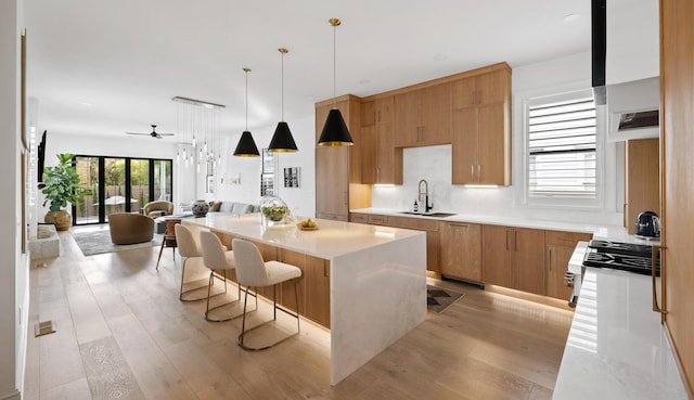 kitchen with light wood-style flooring, a kitchen island, open floor plan, pendant lighting, and a sink