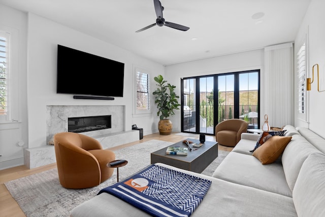 living area with a wealth of natural light, wood finished floors, ceiling fan, and a premium fireplace