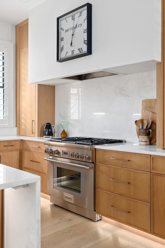 kitchen featuring tasteful backsplash, light wood-type flooring, high end stove, and light countertops