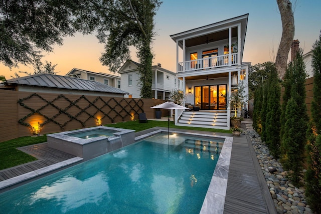 back of house at dusk with a balcony, metal roof, an in ground hot tub, a standing seam roof, and fence