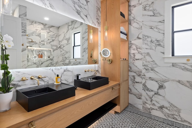 bathroom featuring double vanity, a sink, a marble finish shower, and stone wall