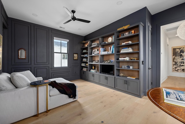 sitting room with a ceiling fan, light wood-type flooring, visible vents, and a decorative wall