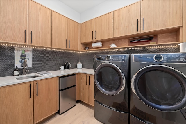 clothes washing area featuring light wood-type flooring, cabinet space, a sink, and independent washer and dryer