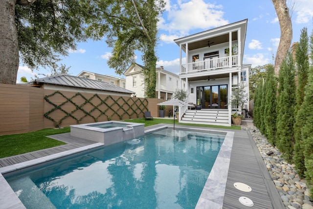 back of house featuring a standing seam roof, ceiling fan, a balcony, an in ground hot tub, and a fenced backyard