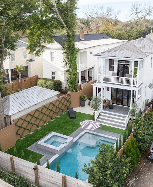 rear view of house with a chimney, a pool with connected hot tub, a balcony, a fenced backyard, and stairs