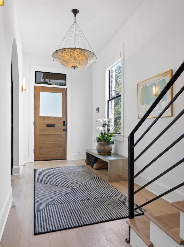 foyer entrance featuring baseboards, stairs, arched walkways, and wood finished floors