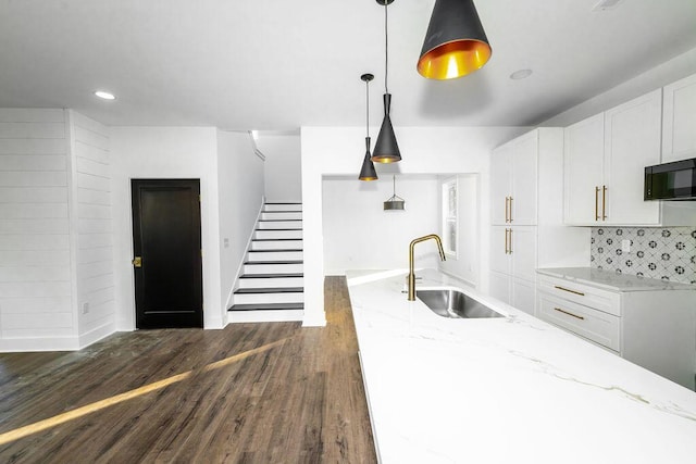 kitchen with black microwave, light stone counters, dark wood-style floors, white cabinets, and a sink