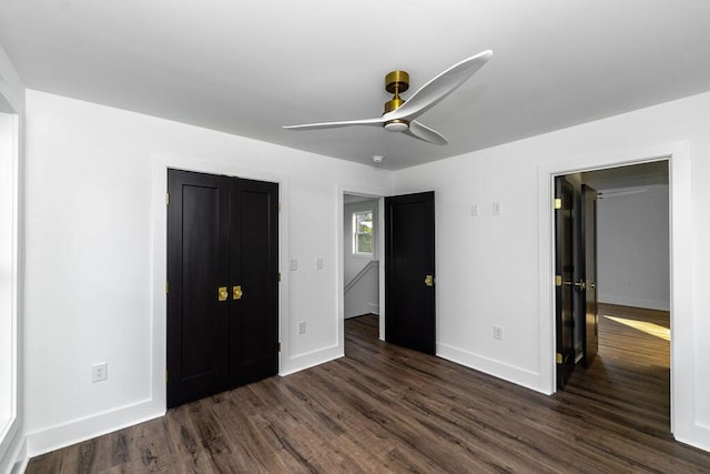 unfurnished bedroom featuring a closet, baseboards, dark wood finished floors, and a ceiling fan