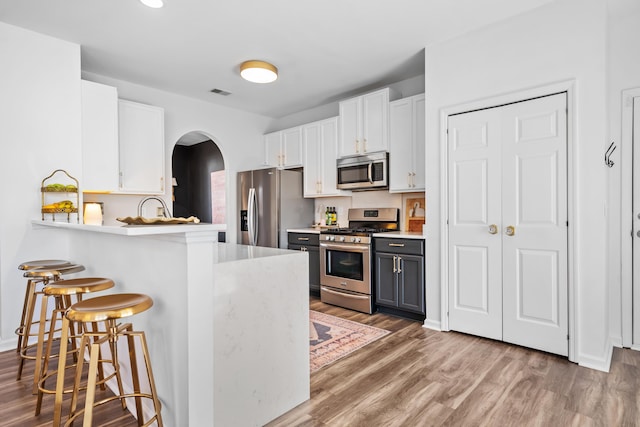 kitchen featuring stainless steel appliances, kitchen peninsula, white cabinets, and a kitchen bar