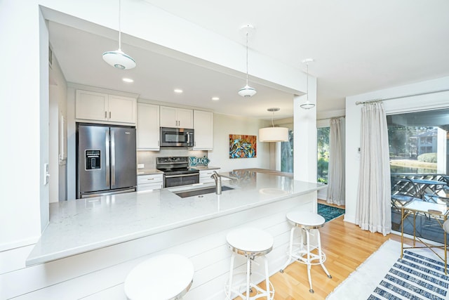 kitchen featuring light wood-type flooring, a kitchen bar, a sink, appliances with stainless steel finishes, and white cabinets