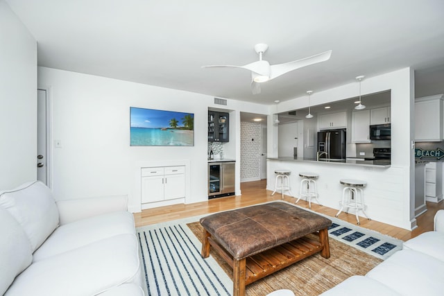 living area featuring a ceiling fan, beverage cooler, visible vents, light wood-style floors, and a dry bar