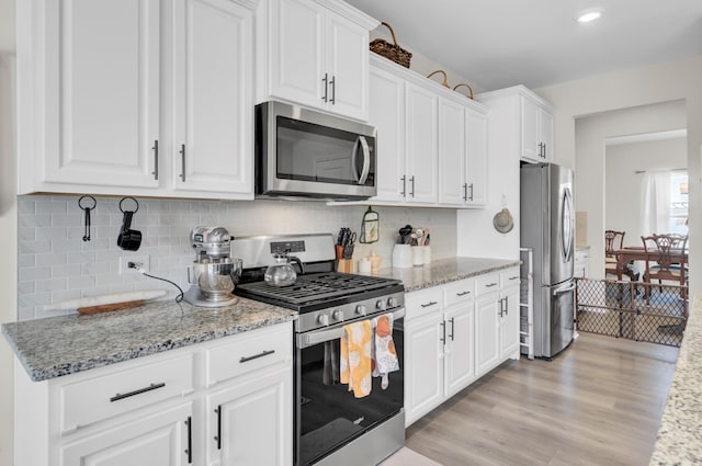 kitchen with white cabinets, light wood-type flooring, stainless steel appliances, and light stone countertops