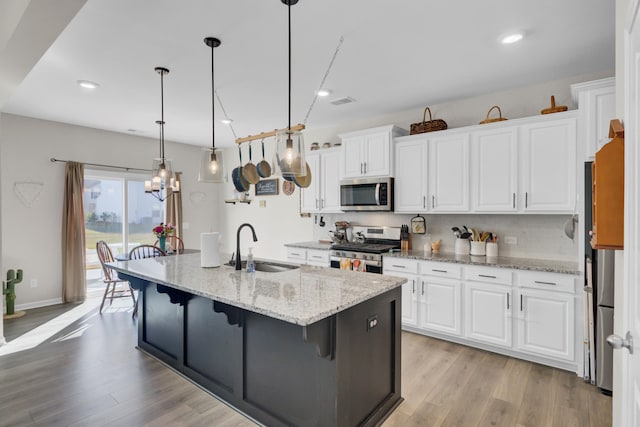 kitchen featuring a center island with sink, white cabinetry, hanging light fixtures, and appliances with stainless steel finishes