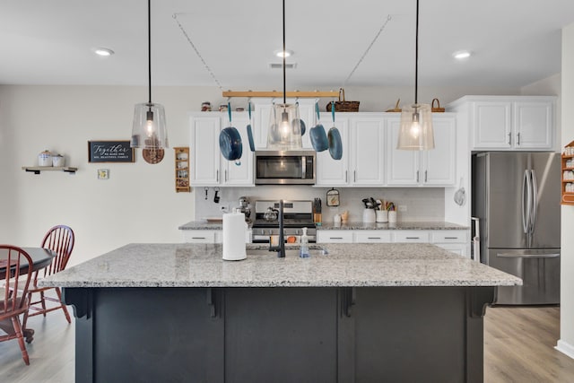 kitchen featuring light wood-type flooring, light stone countertops, hanging light fixtures, and appliances with stainless steel finishes