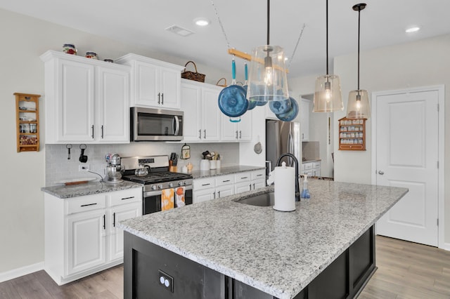 kitchen with sink, stainless steel appliances, pendant lighting, a center island with sink, and white cabinets