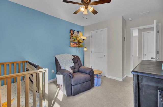 bedroom with ceiling fan, light colored carpet, and a crib