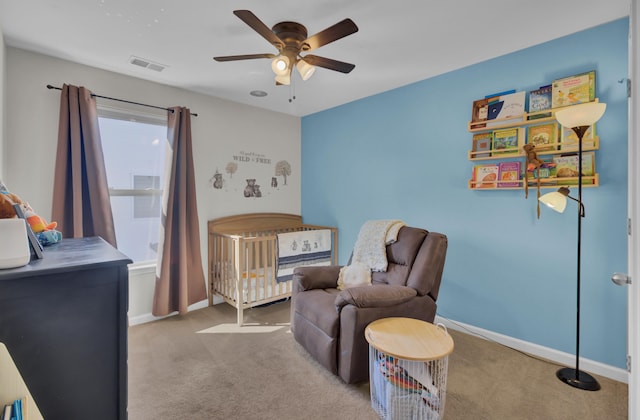 bedroom with a crib, light colored carpet, and ceiling fan