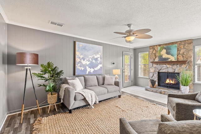 living room featuring wood walls, ornamental molding, ceiling fan, a fireplace, and wood-type flooring