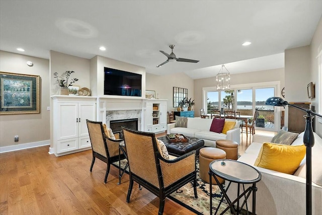 living area with light wood-style flooring, recessed lighting, ceiling fan with notable chandelier, a premium fireplace, and baseboards