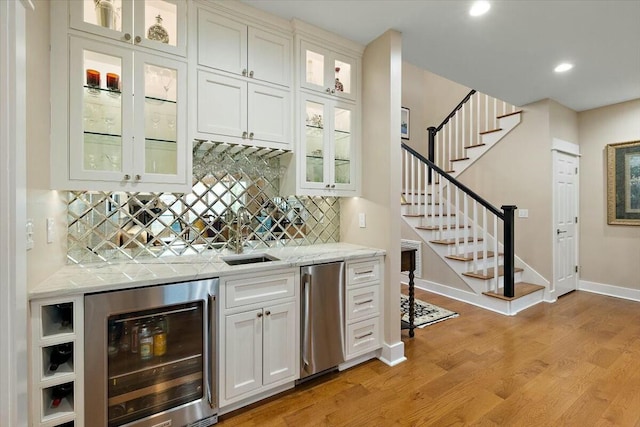 bar with light wood-style flooring, wine cooler, stairway, refrigerator, and wet bar