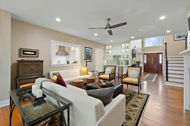 living room featuring ceiling fan, recessed lighting, wood finished floors, baseboards, and stairway