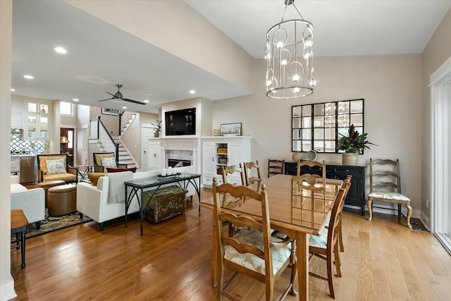 dining space featuring light wood-style flooring, a fireplace, and ceiling fan with notable chandelier