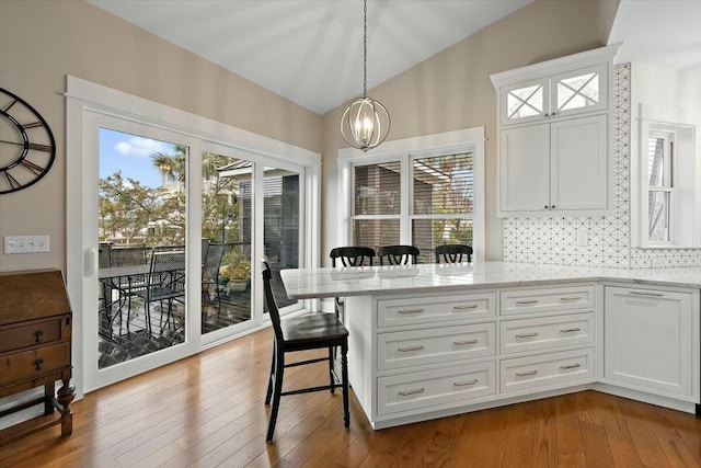 kitchen with white cabinets, vaulted ceiling, light stone countertops, a peninsula, and a kitchen breakfast bar