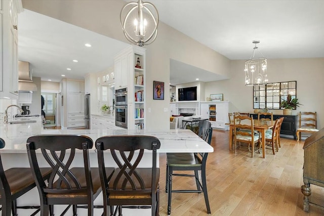 kitchen featuring a fireplace, hanging light fixtures, an inviting chandelier, white cabinets, and a peninsula