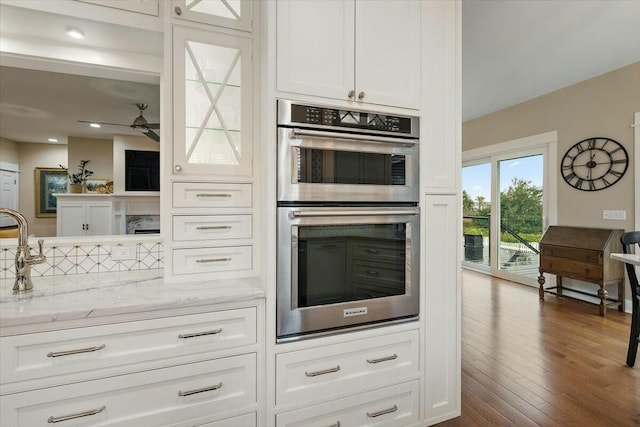 kitchen with light stone counters, stainless steel double oven, white cabinetry, decorative backsplash, and dark wood finished floors