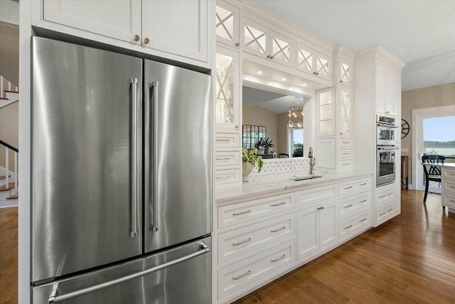 kitchen featuring appliances with stainless steel finishes, dark wood-type flooring, white cabinetry, a sink, and light stone countertops