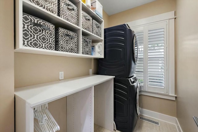 laundry room with stacked washer and clothes dryer, light tile patterned floors, visible vents, laundry area, and baseboards