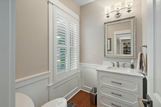 bathroom featuring visible vents, a decorative wall, wainscoting, vanity, and wood finished floors