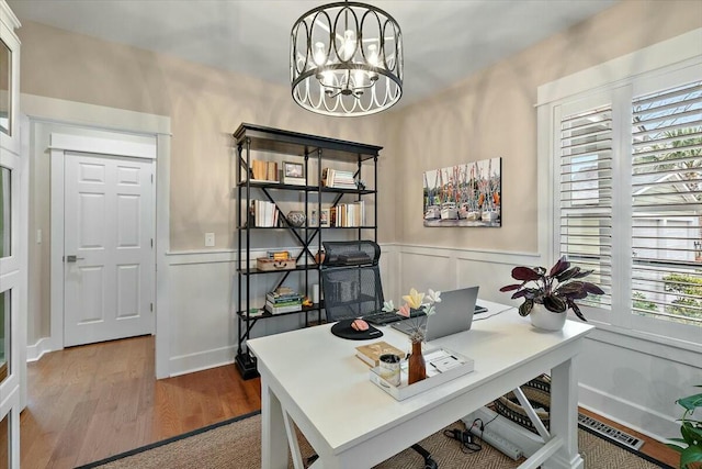 home office featuring light wood-type flooring, a wainscoted wall, visible vents, and an inviting chandelier