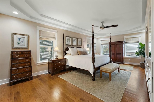 bedroom with dark wood-style floors, a raised ceiling, and multiple windows