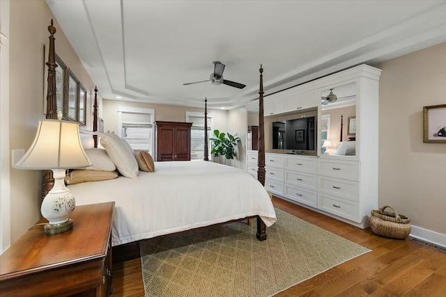 bedroom with baseboards, visible vents, a ceiling fan, wood finished floors, and a tray ceiling