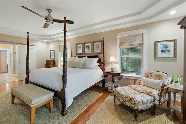 bedroom featuring a barn door, a tray ceiling, wood finished floors, and recessed lighting