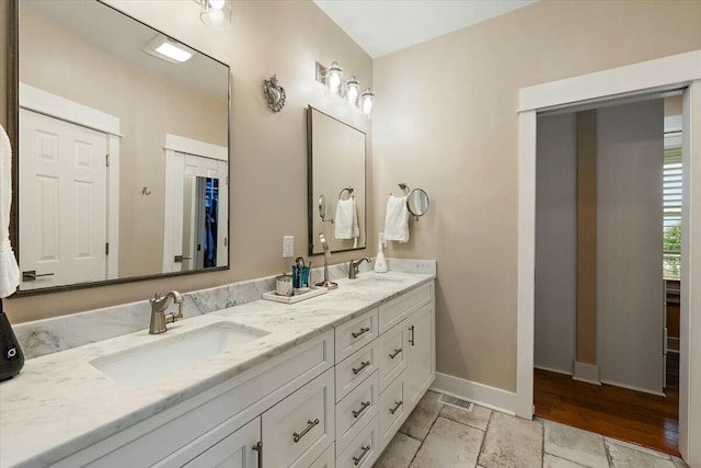 full bath featuring double vanity, a sink, visible vents, and baseboards