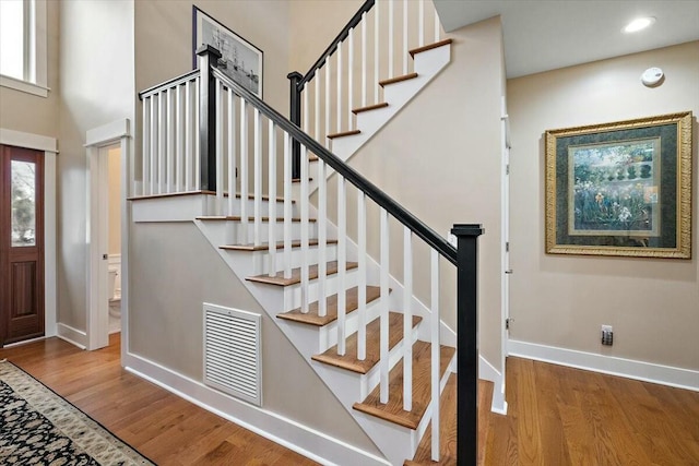 entryway featuring recessed lighting, wood finished floors, a towering ceiling, visible vents, and baseboards